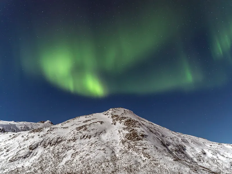 A snowy mountain with the aurora dancing above